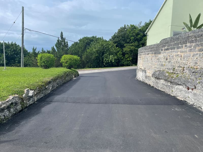 Newly paved access driveway between a limestone wall and a grass bank