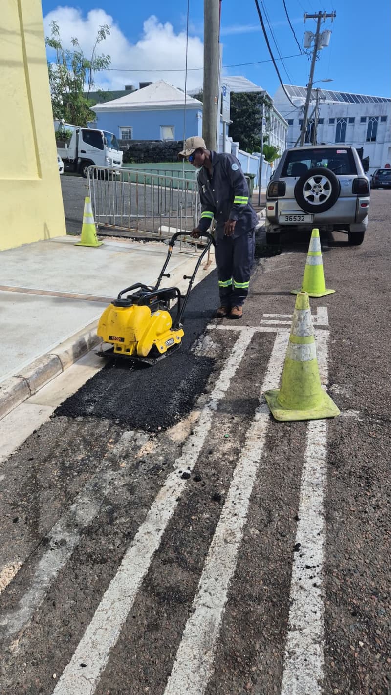 Quality Control Ltd crew member compacting a fresh asphalt patch along a curb with a plate compactor