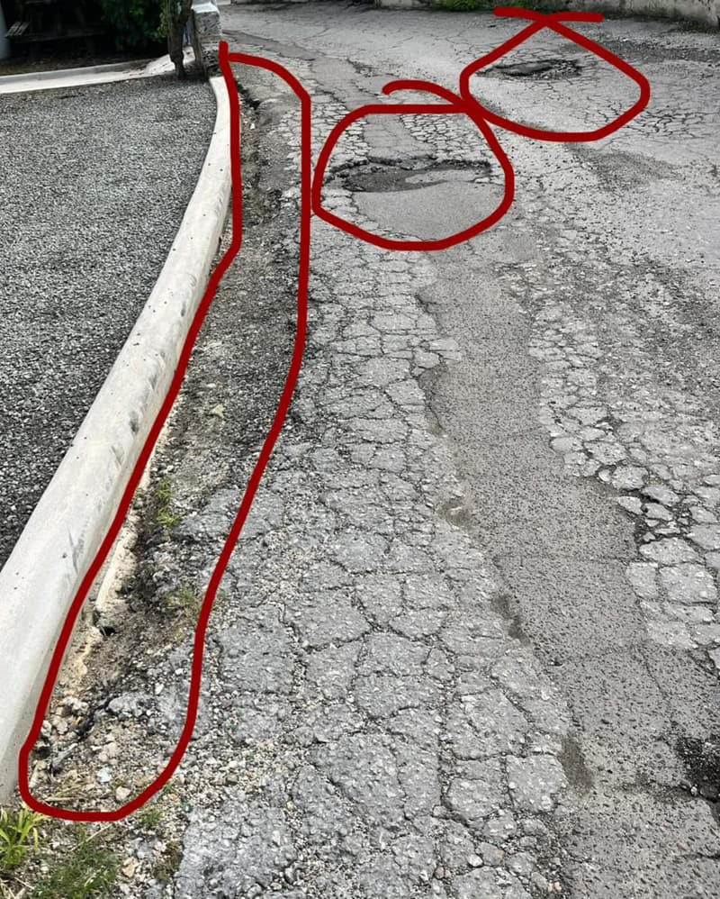 Cracked asphalt with potholes and a broken edge along a curb, damaged areas circled in red