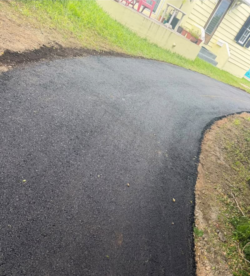 Freshly paved asphalt driveway curving up to a yellow Bermuda home