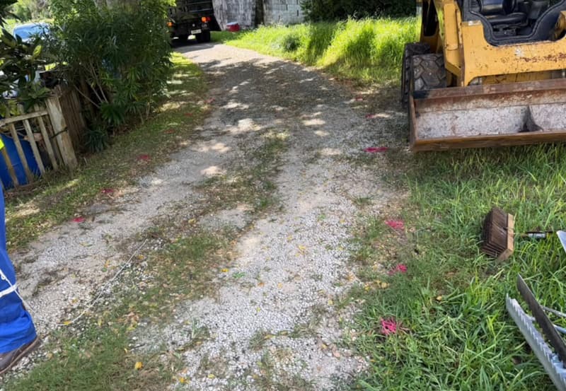 Gravel driveway with grass growing through before paving, with a skid steer on site