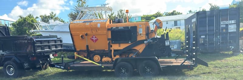 Quality Control asphalt paver loaded on a trailer next to a dump truck