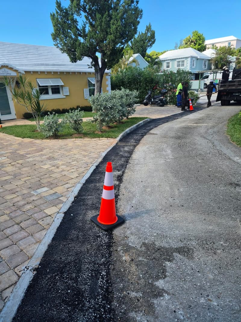 New asphalt ramp along a curved driveway curb, with safety cone and crew working beyond