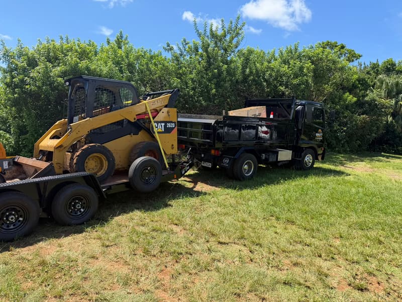 Quality Control Ltd branded dump truck towing a CAT skid steer