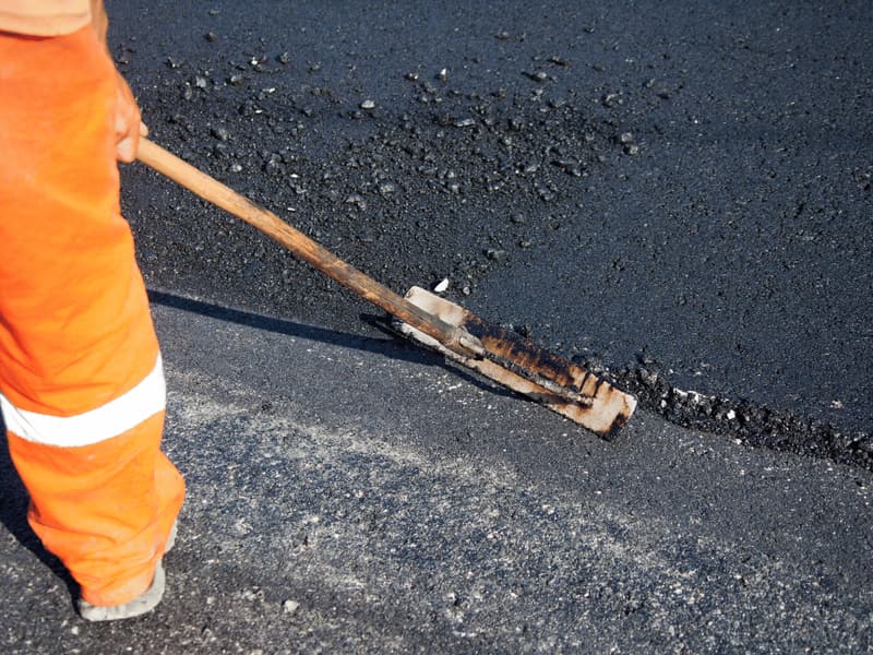 Worker levelling the edge of freshly laid asphalt