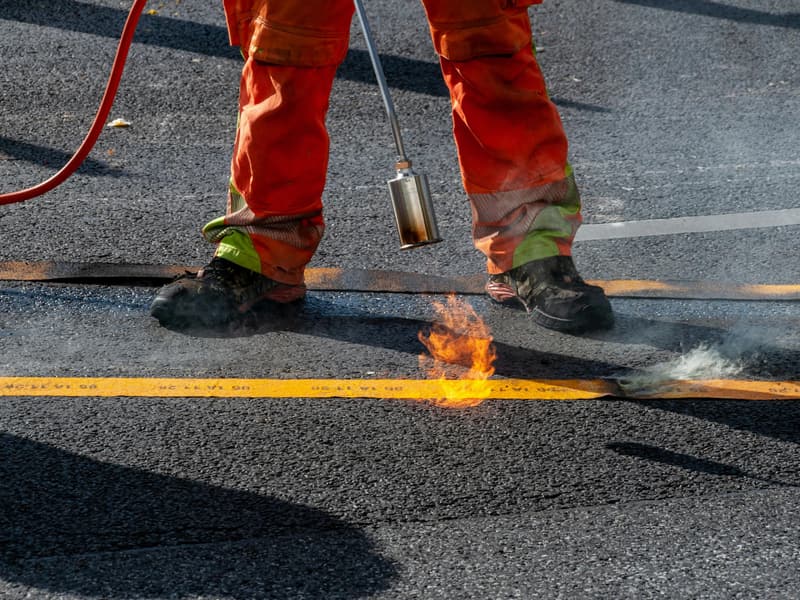 Worker applying a yellow line marking to an asphalt road surface