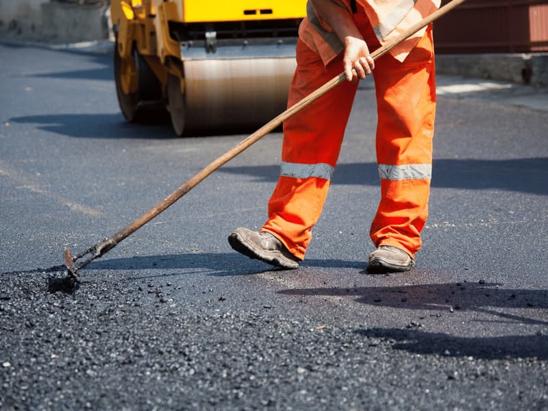 Worker raking fresh asphalt in front of a roller