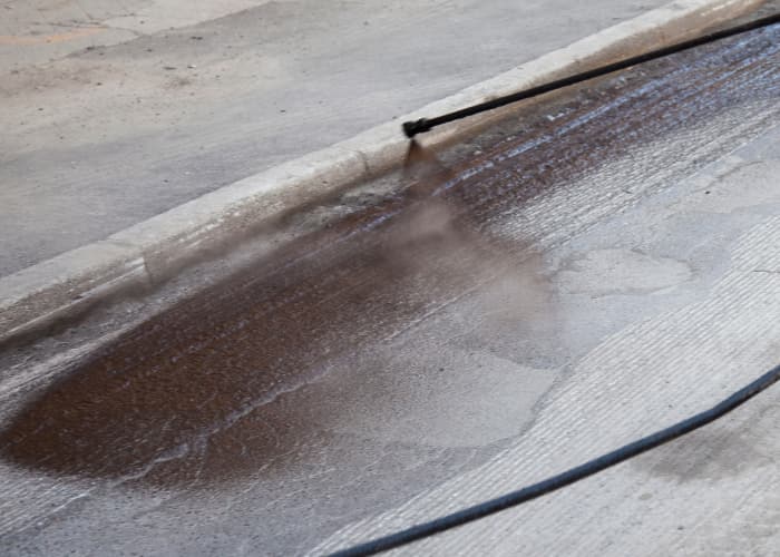 Sealer being sprayed across a paved surface beside a curb