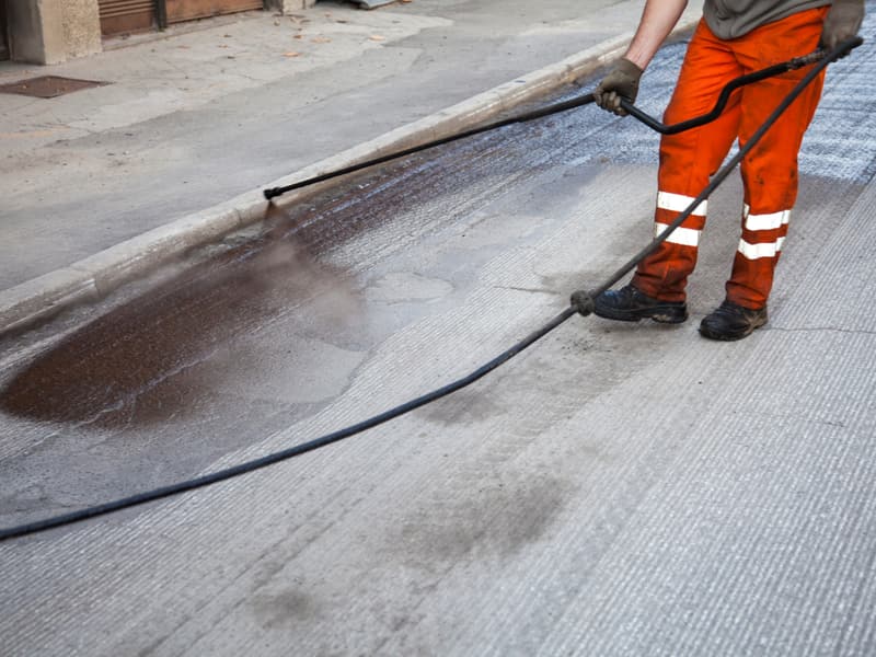 Worker spray-applying sealer to an asphalt surface